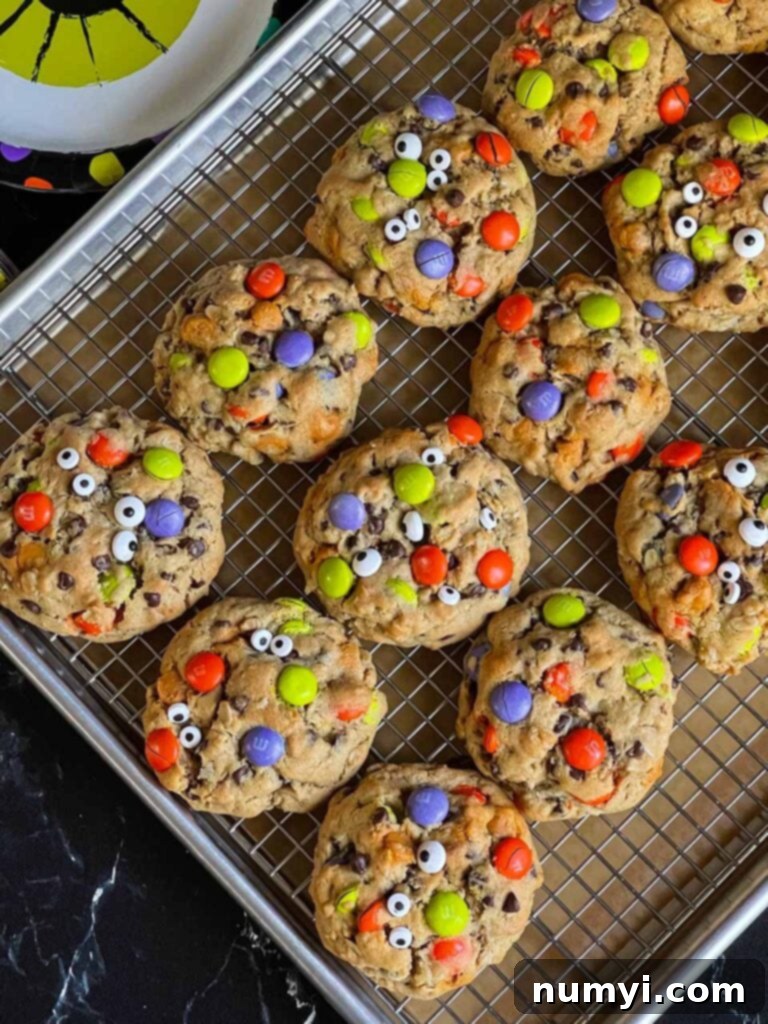 More Halloween monster cookies with various candy eyes on a wire rack within a baking sheet.