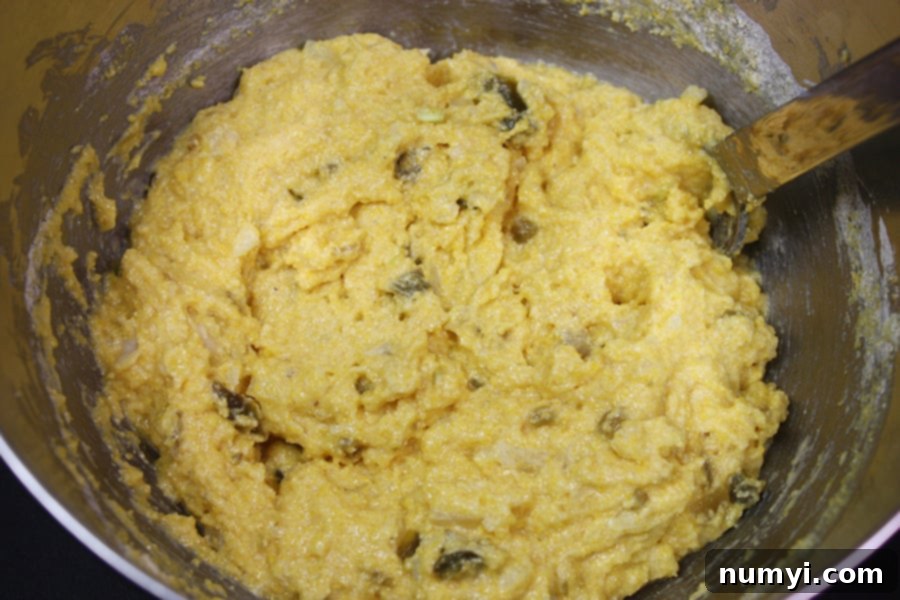 Close-up of the thick, textured Jalapeno Hushpuppies batter in a shining metal mixing bowl, ready for frying.