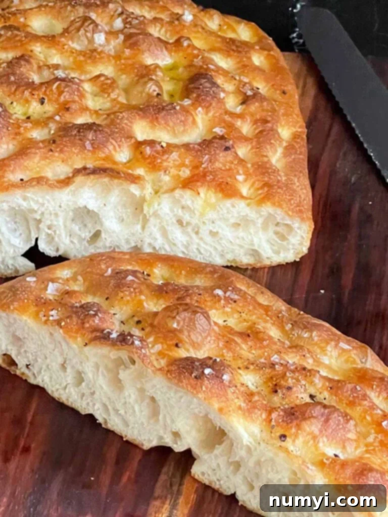 Fresh baked overnight focaccia cut in half on a wooden cutting board.