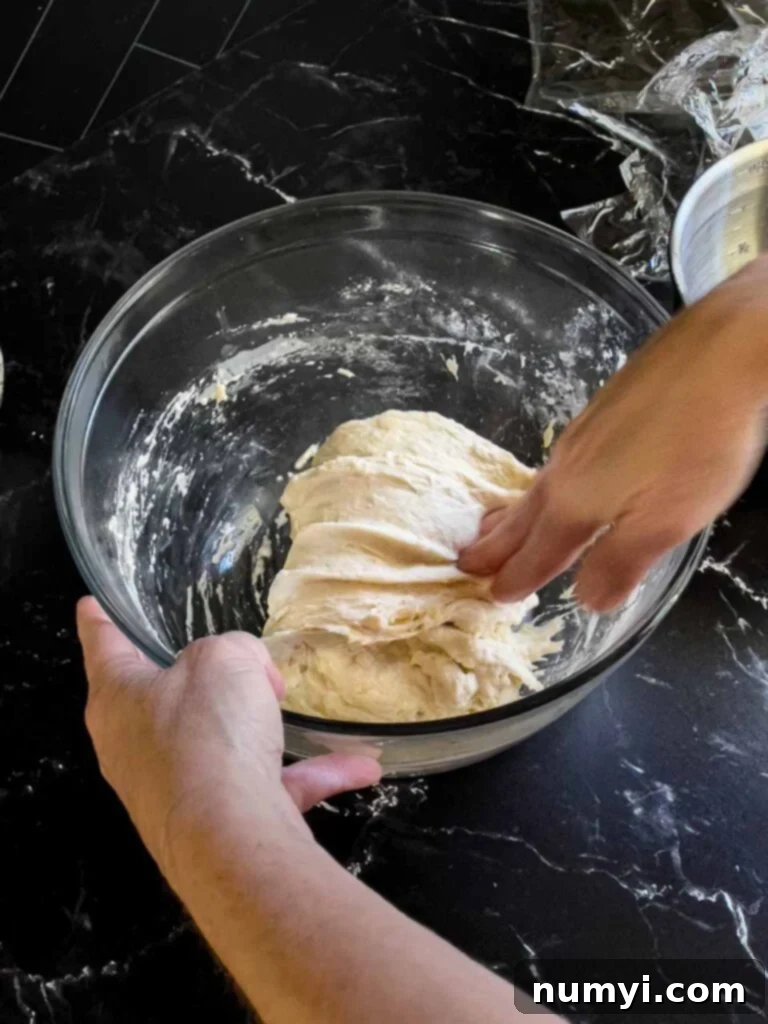 Stretching and folding the focaccia bread dough in a glass bowl.