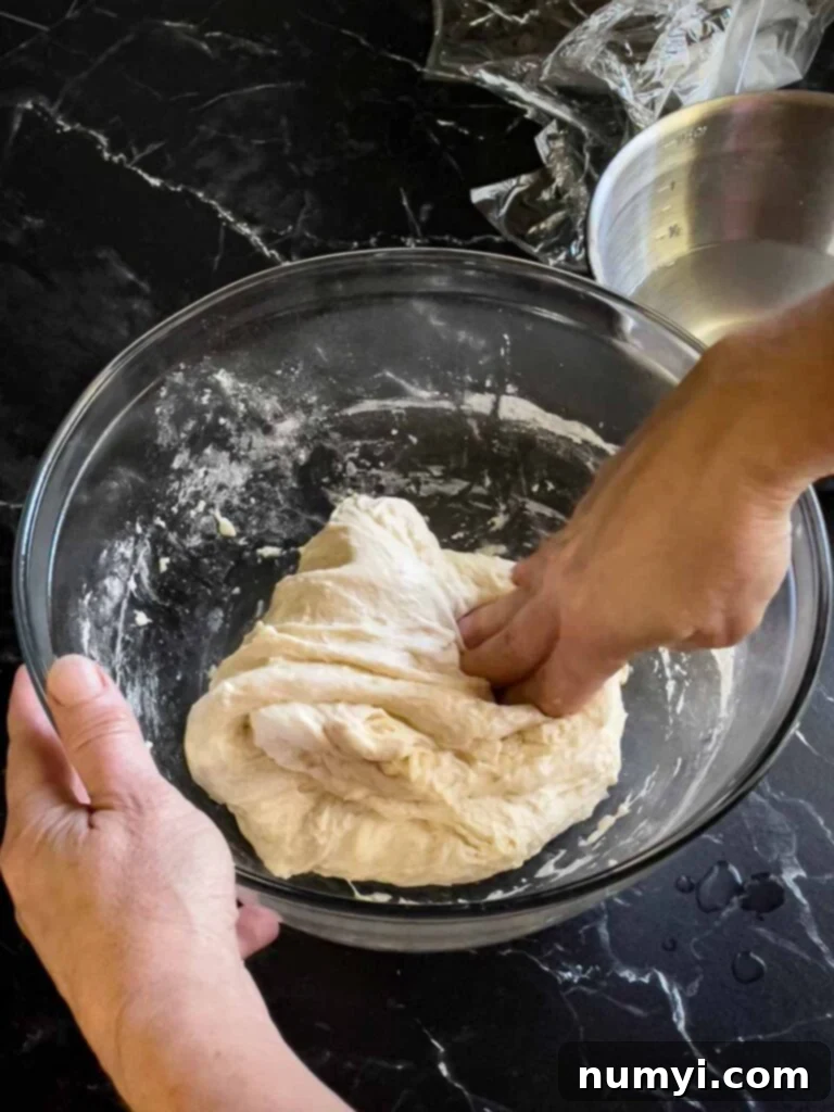 Stretching and folding the focaccia dough a second time in a glass bowl.