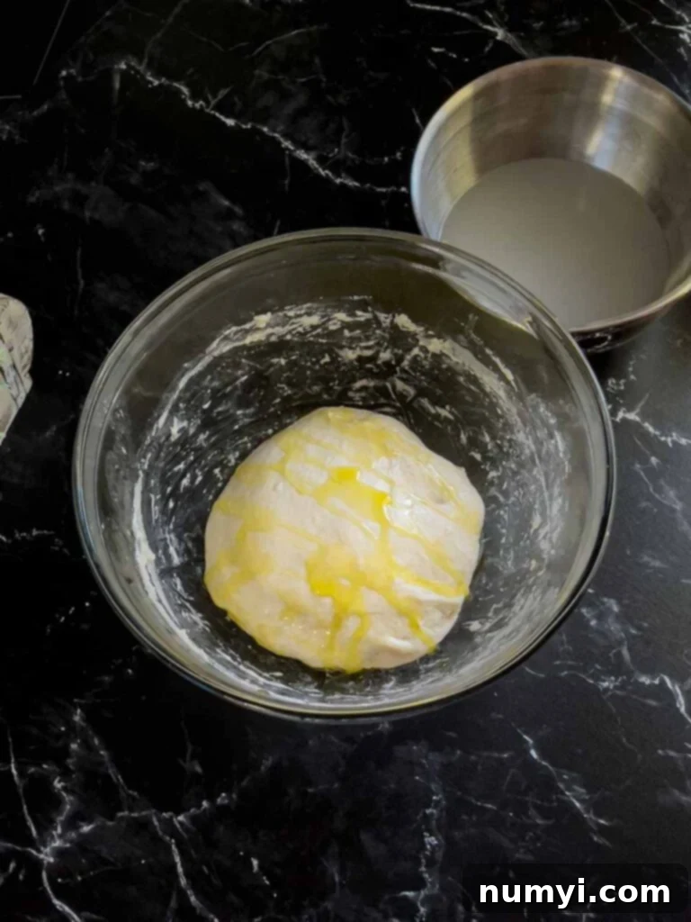 Focaccia dough, topped with olive oil, in a glass bowl.