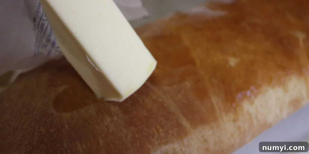Bake Perfect Homemade Sandwich Bread 13 Warm, golden crust of homemade sandwich bread being rubbed with butter for added shine and softness.