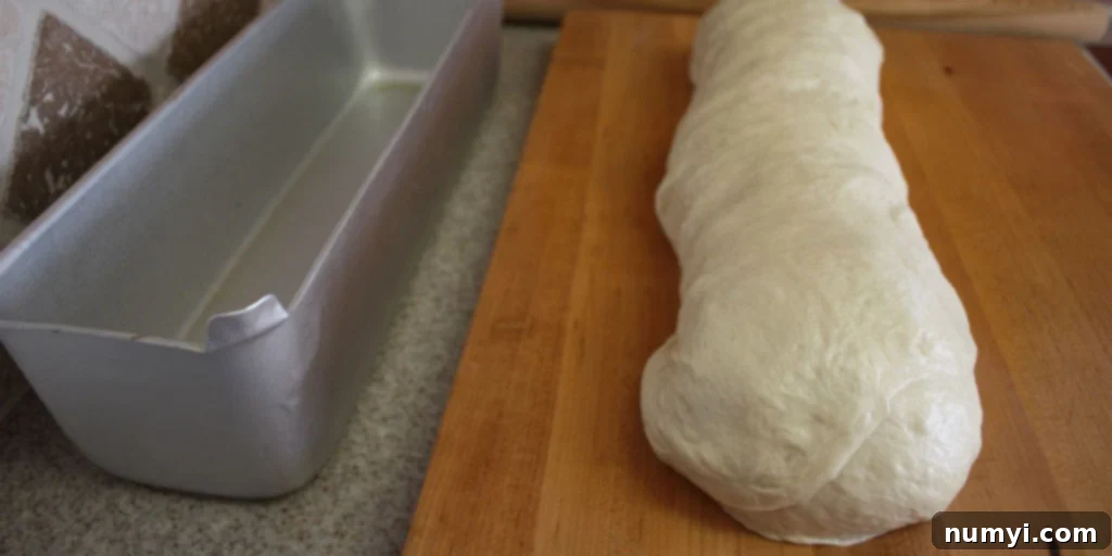 Bake Perfect Homemade Sandwich Bread 8 Neatly shaped sandwich bread dough, rolled into a loaf and resting on a wooden board.