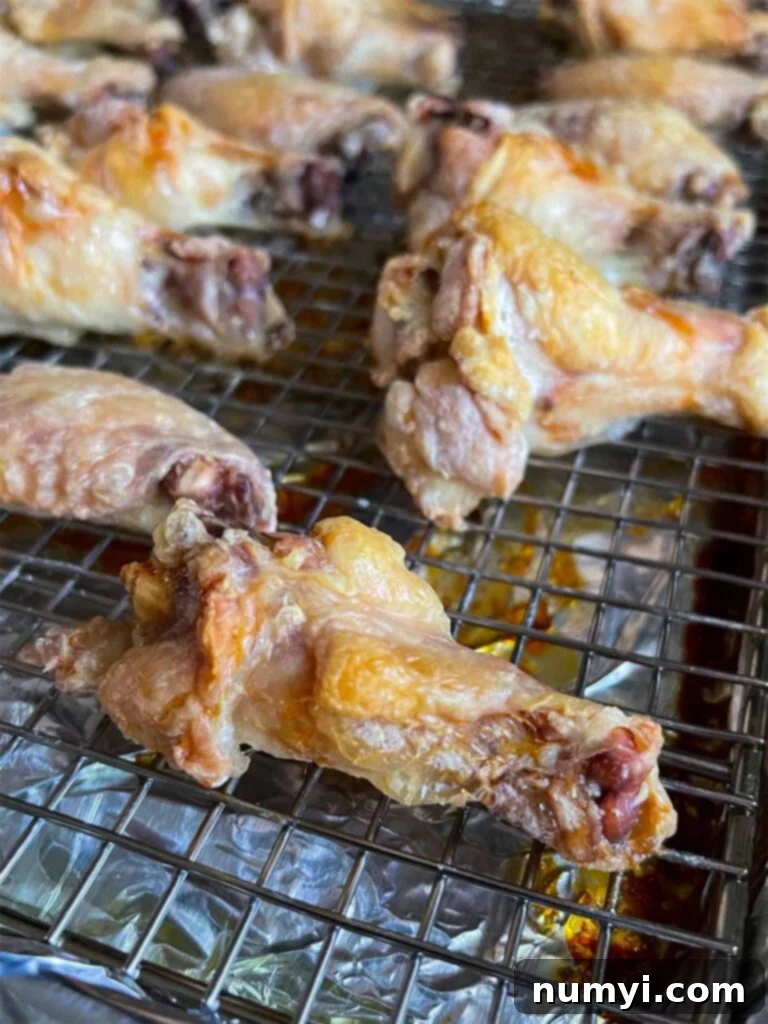 Freshly baked chicken wings with a golden-brown, crispy skin, resting on a wire rack after the initial baking phase, looking perfectly rendered.