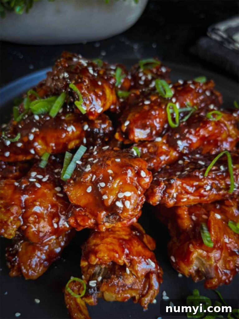 A vibrant plate of finished Asian chicken wings on a sleek black plate, artfully garnished with a generous sprinkle of green onions and sesame seeds, showcasing their delicious glaze and vibrant colors.