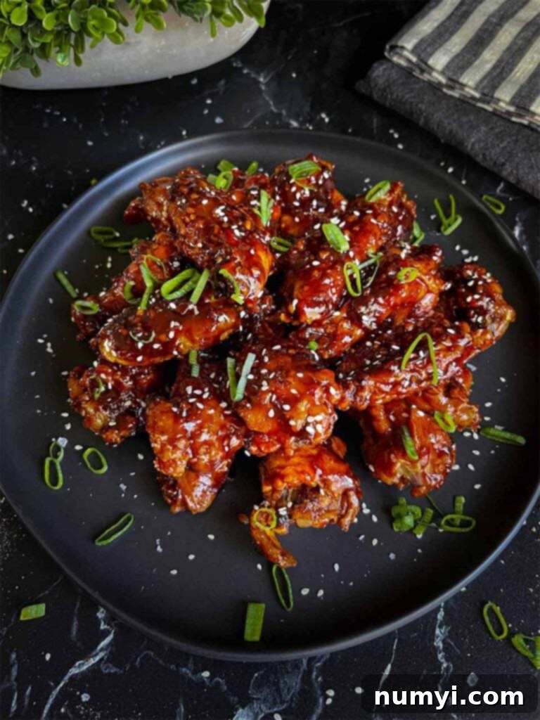 An appetizing close-up of a plate of Asian chicken wings, artfully adorned with finely chopped green onions and sesame seeds, showcasing their delicious glaze and inviting texture.
