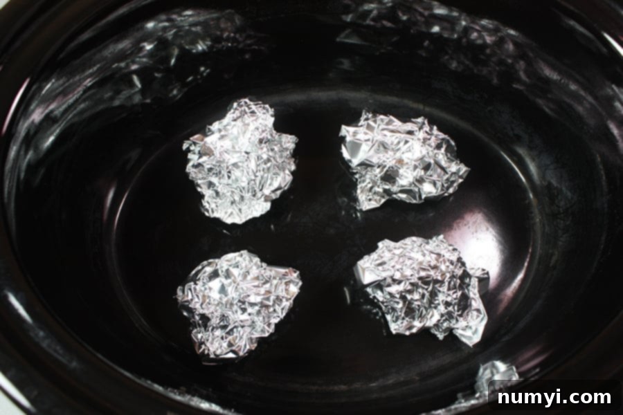 Perfectly Tender Slow Cooker Roasted Chicken 4 Small balls of aluminum foil arranged as a rack inside the crock of a slow cooker.