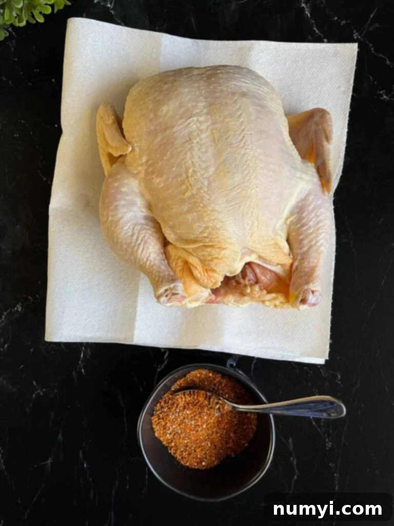 Perfectly Tender Slow Cooker Roasted Chicken 5 Raw whole chicken on paper towels with a small bowl of spice rub, ready for seasoning.