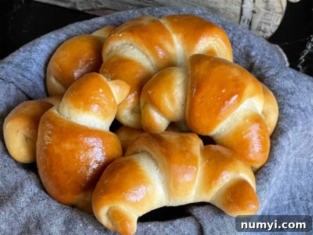 Freshly baked golden crescent rolls nestled in a bread basket lined with a gray towel, ready to be served.