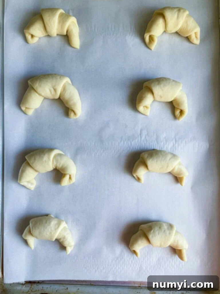 Unbaked crescent rolls arranged on a parchment paper-lined baking sheet, ready for the oven.
