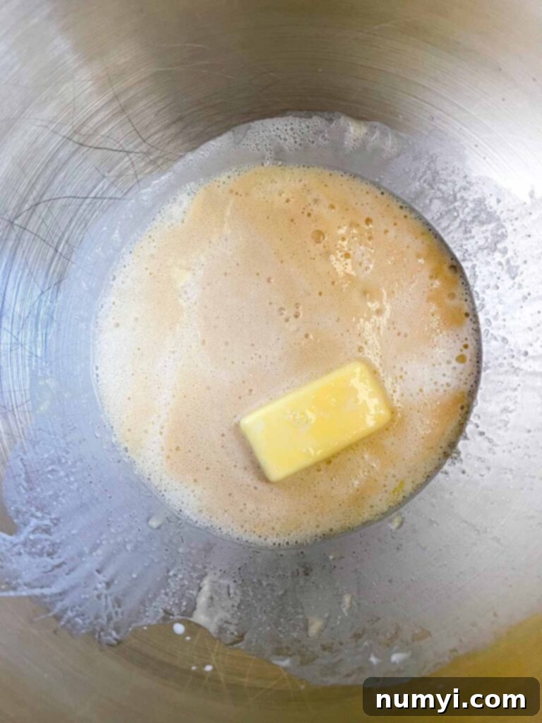 The liquid ingredients, including warm milk and melted butter, for crescent roll dough in a metal bowl.