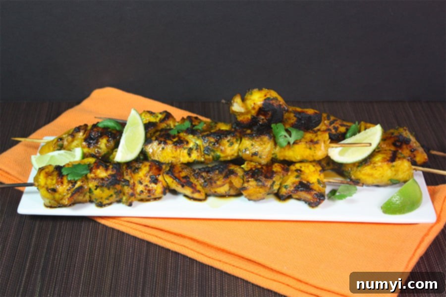 Golden Spice Chicken Skewers 2 Turmeric chicken skewers on a white serving plate garnished with fresh herbs and lime wedges.