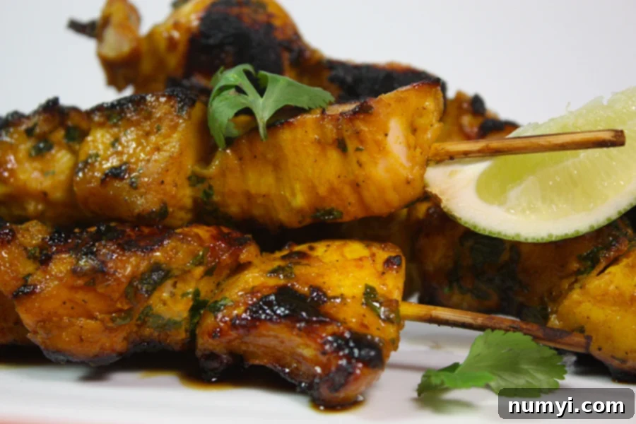 Golden Spice Chicken Skewers 5 Cooked Turmeric Chicken Kabobs on a white platter garnished with fresh parsley and lime wedges.
