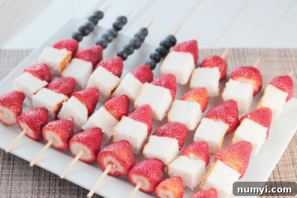 eight fruit kabobs made of strawberries, blueberries, and angel food cake displayed on a white serving plate