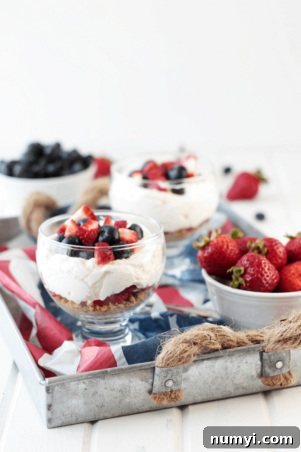 a couple bowls of cheesecake parfait with berries served on a tray with American flag decor and bowls of fresh berries