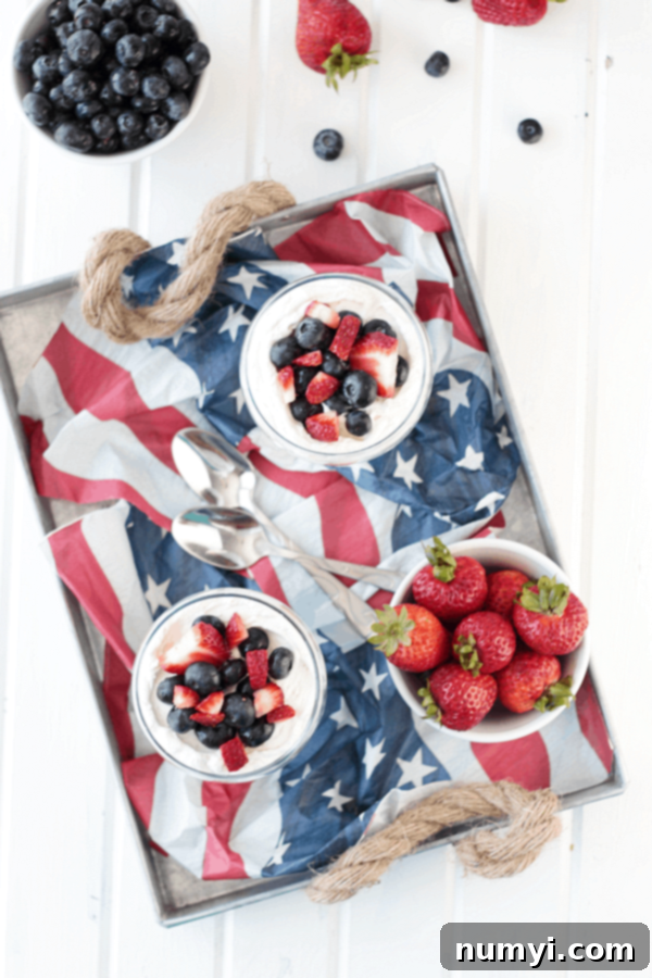 an overhead shot of an american flag in a serving platter with bowls of cheesecake parfait and fresh berries on it