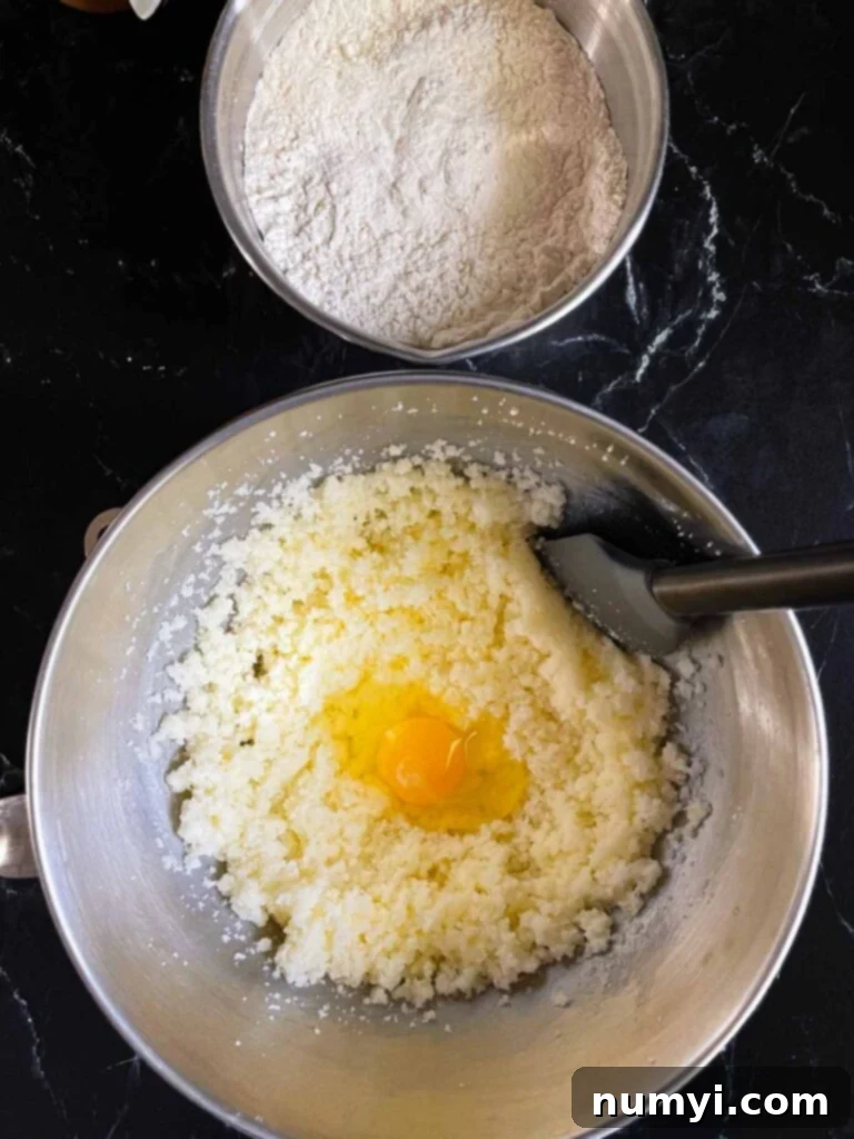 Eggs being added to one at a time to the creamed butter and sugar in a metal mixing bowl.