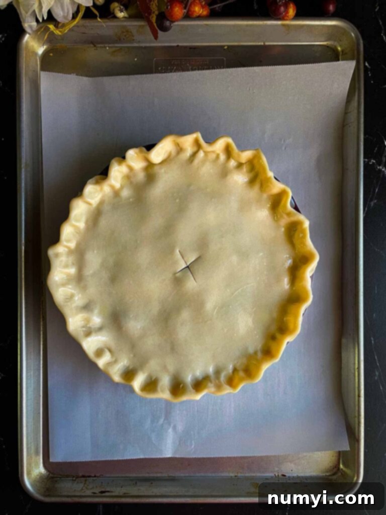 Thanksgiving Encore Pie 10 An assembled Thanksgiving leftovers pie, with a crimped top crust and egg wash, positioned on a foil-lined baking sheet and ready for the oven.