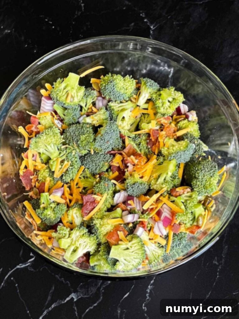 Broccoli salad ingredients tossed in a large glass mixing bowl.