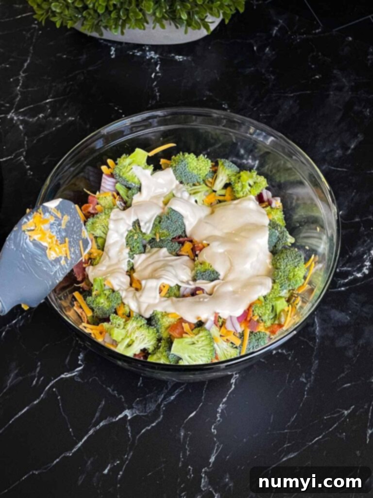 Dressing poured over the broccoli salad ingredients in a glass bowl.