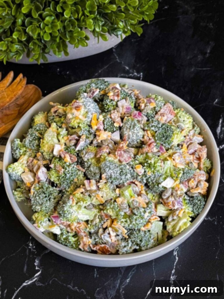 Broccoli salad in a light bowl with a plant in the background.