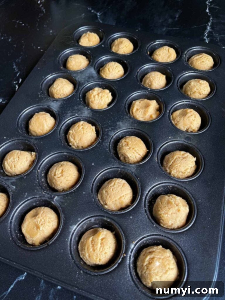 Chocolate Peanut Butter Cup Cookies 6 Small, uniform balls of peanut butter cookie dough placed neatly into the cavities of a greased mini muffin pan, ready for baking.