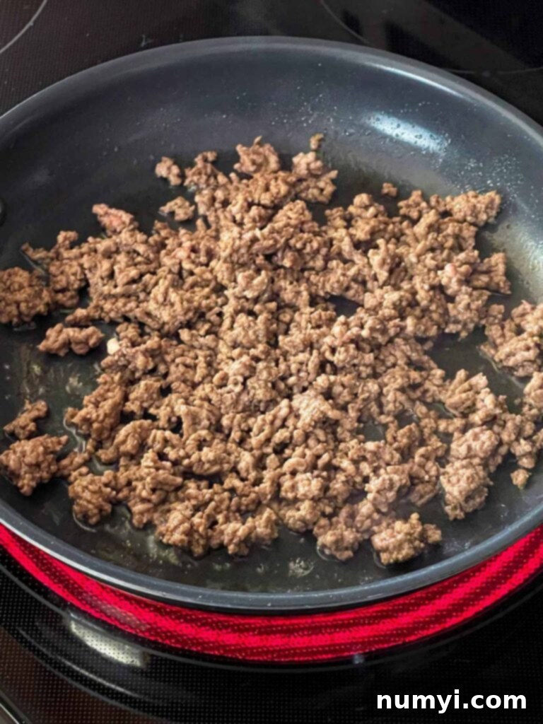 Molten Beef & Cheese Dip 5 Ground beef cooking in a skillet, being broken apart with a wooden spoon.