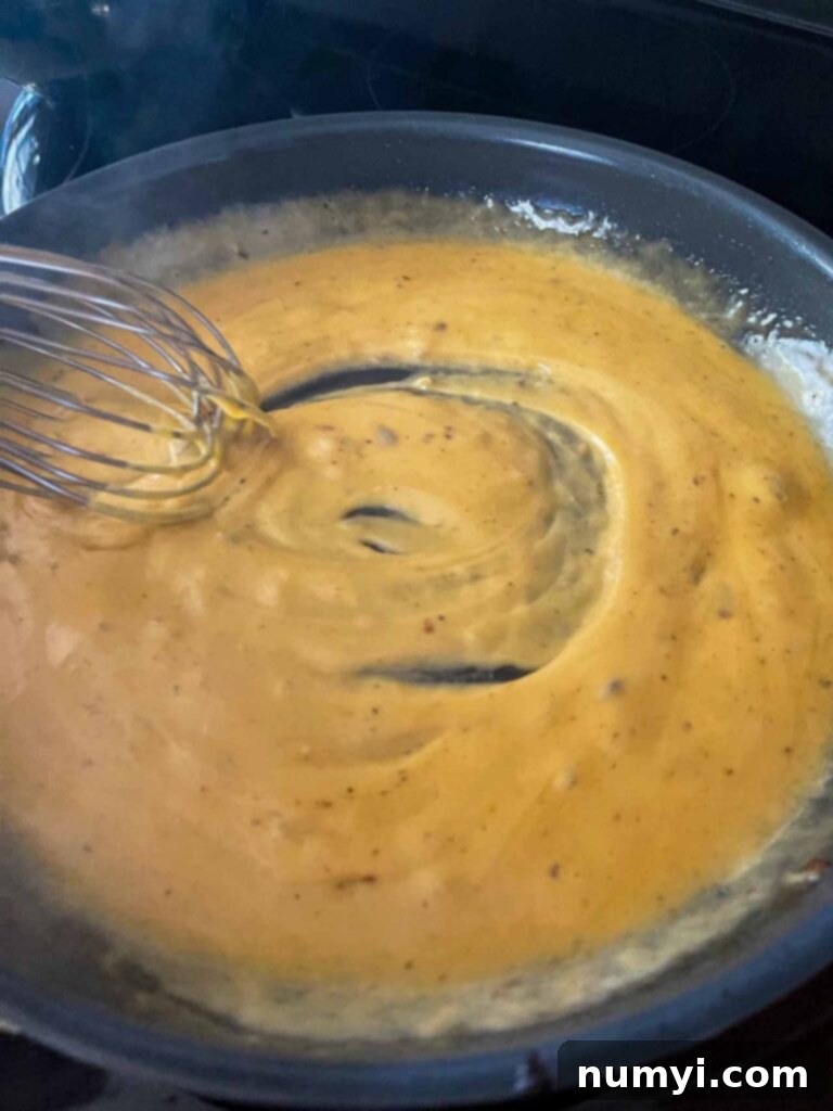 Molten Beef & Cheese Dip 8 Cheese sauce being whisked in a skillet, showing its smooth, creamy texture.