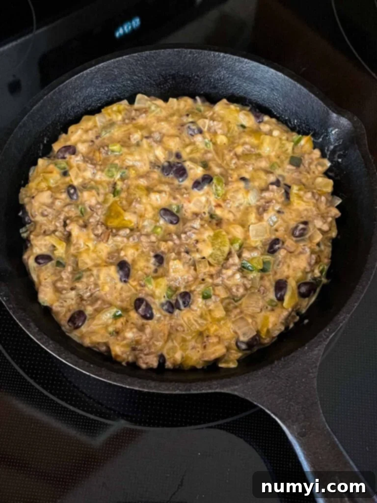 Molten Beef & Cheese Dip 9 Queso Fundido mixture in a cast iron skillet, ready to be baked in the oven until bubbly.