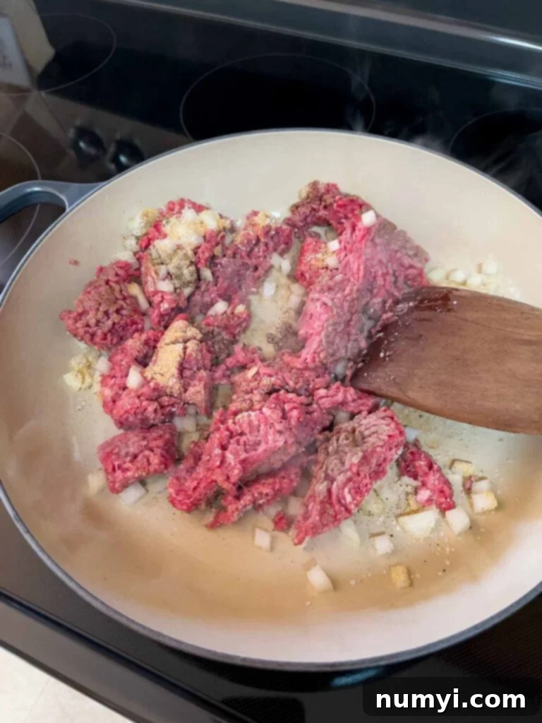 Ground beef and diced yellow onions cooking in a cast iron skillet, starting to brown beautifully.