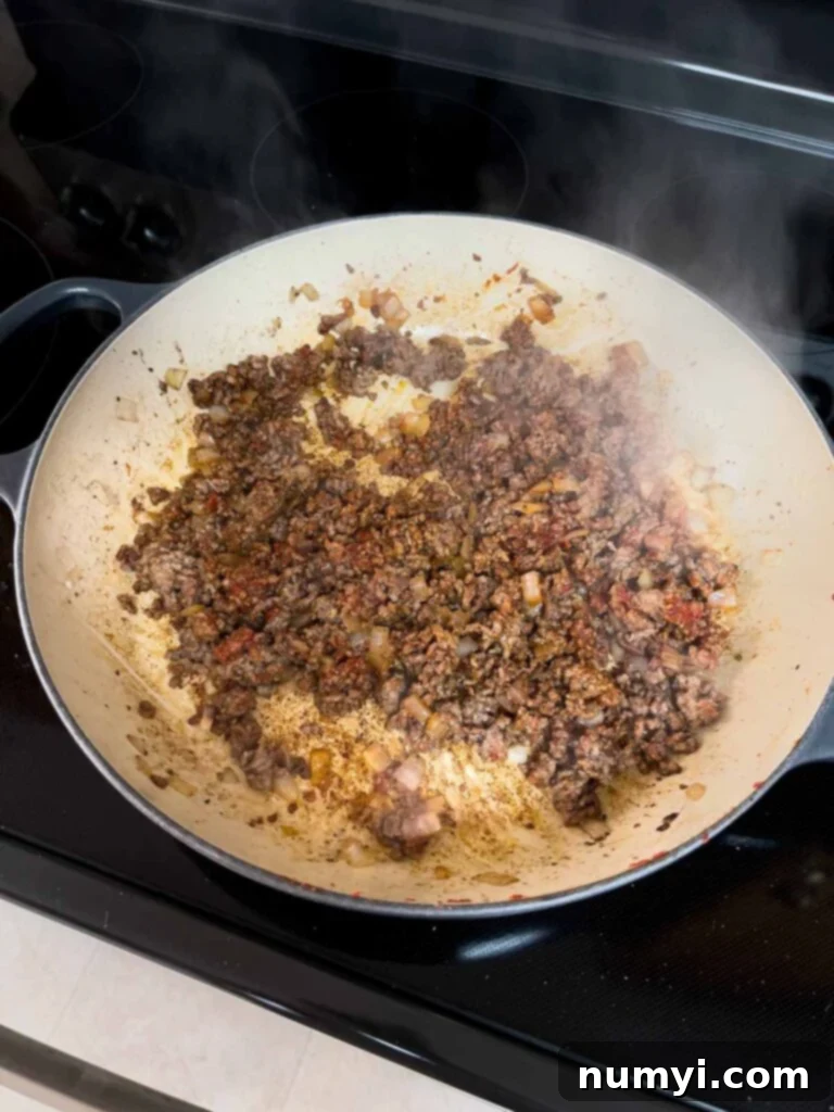 Cooked and seasoned ground beef with onions in a cast iron skillet, ready for the next steps.