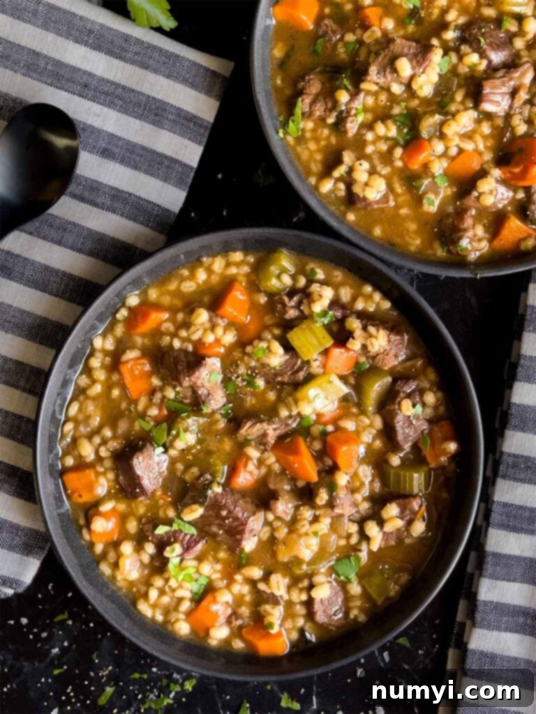 Beef barley soup in two dark bowls with striped napkins next to them.