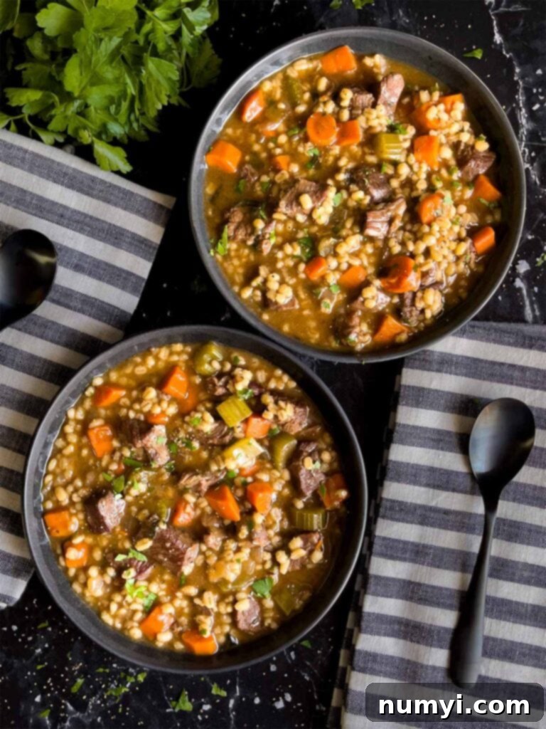 Beef barley soup in two dark bowls with striped napkins next to them.