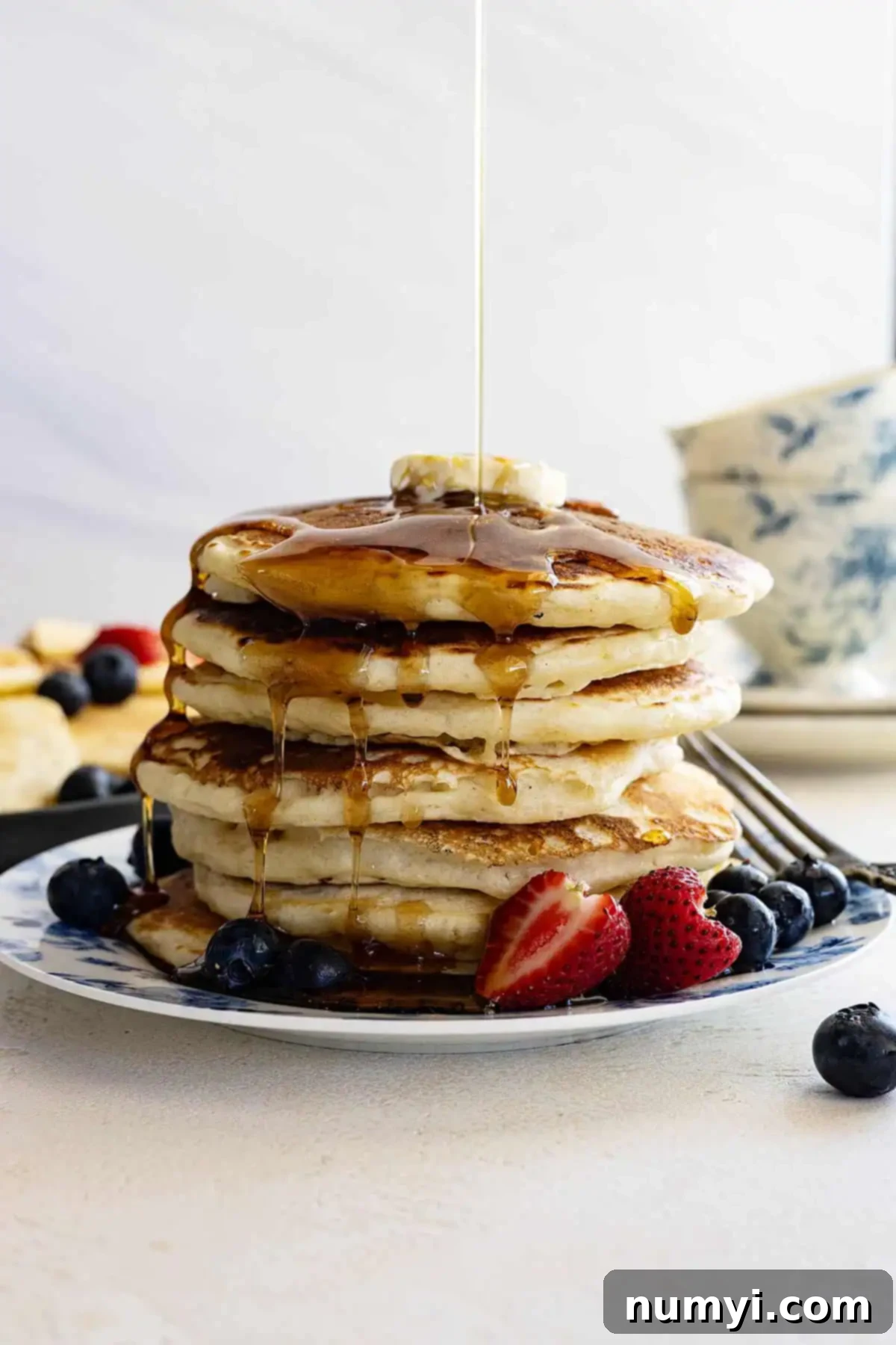 Easy-Fluffy-Pancakes-picture Tall stack of golden brown, fluffy pancakes with a pat of butter melting on top and rich maple syrup being poured over.