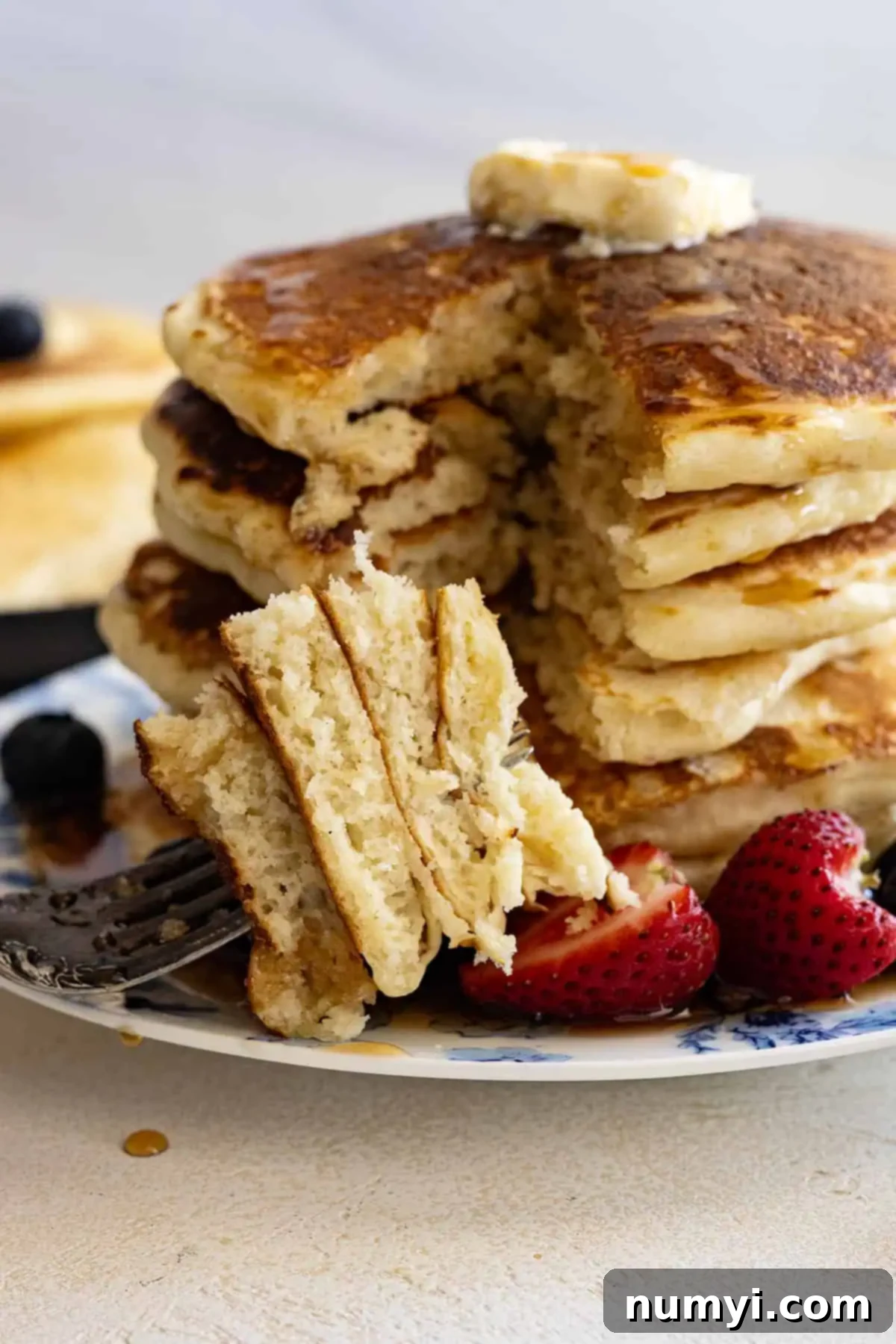 Effortless Fluffy Homemade Pancakes 5 A close-up shot of a tall stack of golden-brown fluffy pancakes, with a fork holding a bite-sized piece in front, showing the airy interior texture.