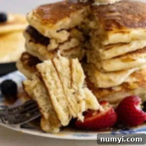 Effortless Fluffy Homemade Pancakes 6 Tall stack of pancakes with a bite taken out on a fork laid in front of the stack.