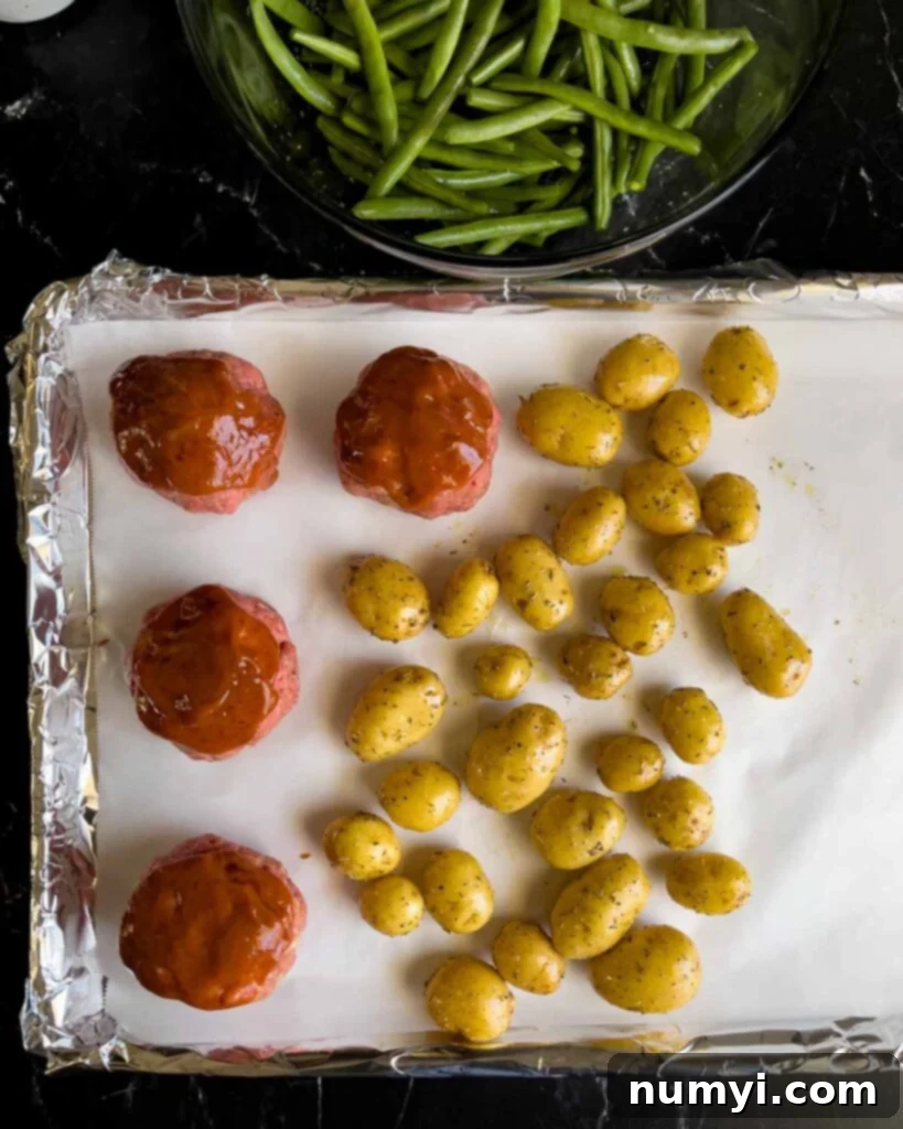 Potatoes added to the sheet pan with the mini meatloaves with the green beans in the background.