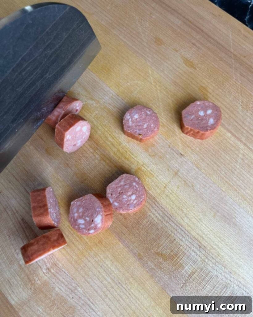 Smoked Bacon Sausage Bites 5 A sharp knife slicing smoked sausage into uniform half-inch rounds on a cutting board.