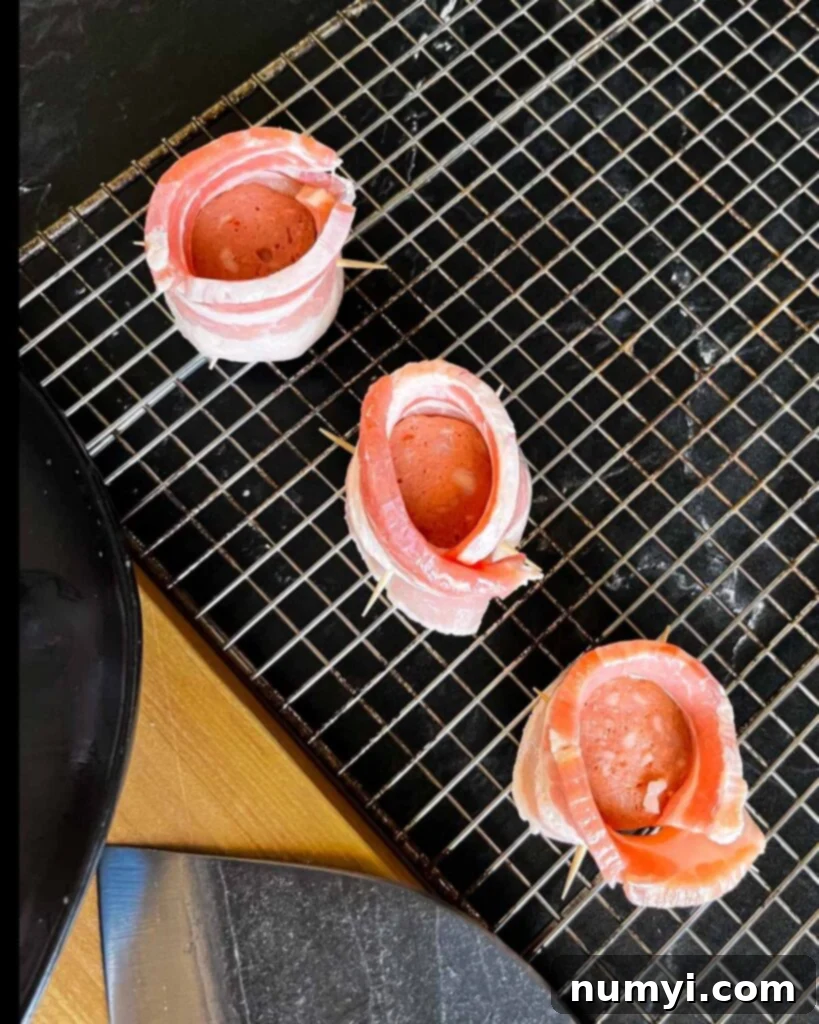 Smoked Bacon Sausage Bites 7 Assembled pig shots showing bacon wrapped around sausage and secured with toothpicks, laid out on a cooling rack.