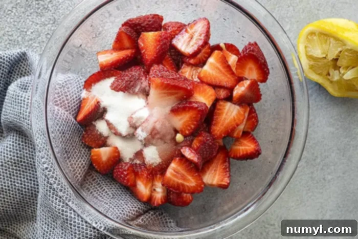 An overhead view of vibrant red strawberries in a bowl, gently macerating with sugar, releasing their sweet juices.