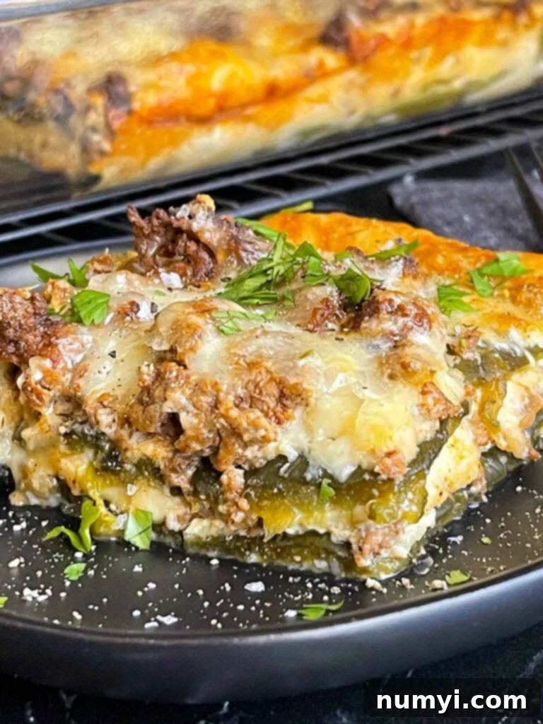 The Ultimate Chile Relleno Casserole 2 A serving of chile relleno casserole on a dark plate with the casserole in the background.