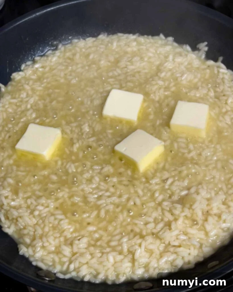 Velvety Mushroom Risotto 15 Butter being added to the creamy risotto in a skillet and stirred.