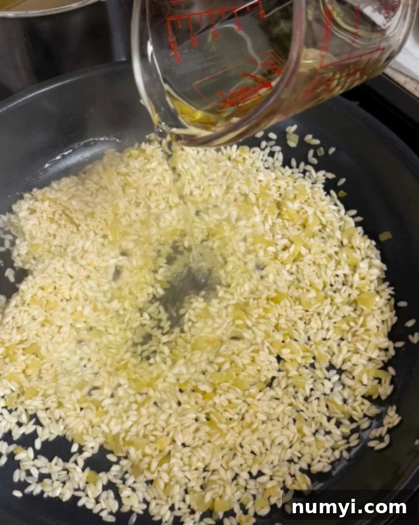 Velvety Mushroom Risotto 8 White wine being poured into the skillet with toasted risotto rice.