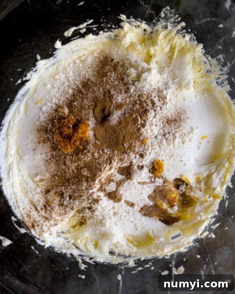 Granulated sugar, cinnamon, flour, orange zest, vanilla extract, and salt added to the whipped mascarpone and ricotta mixture in a glass bowl.