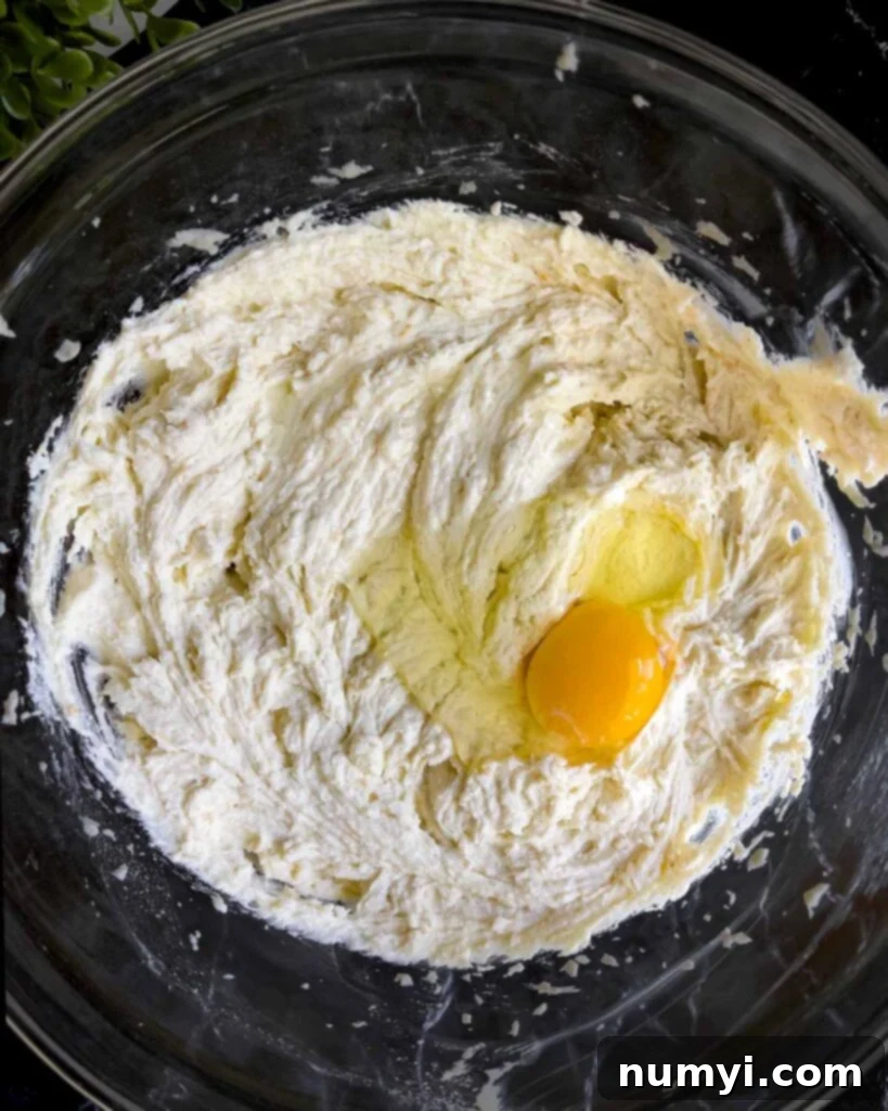 Eggs being carefully added one by one to the cannoli cheesecake mixture in a glass bowl, ensuring smooth incorporation.