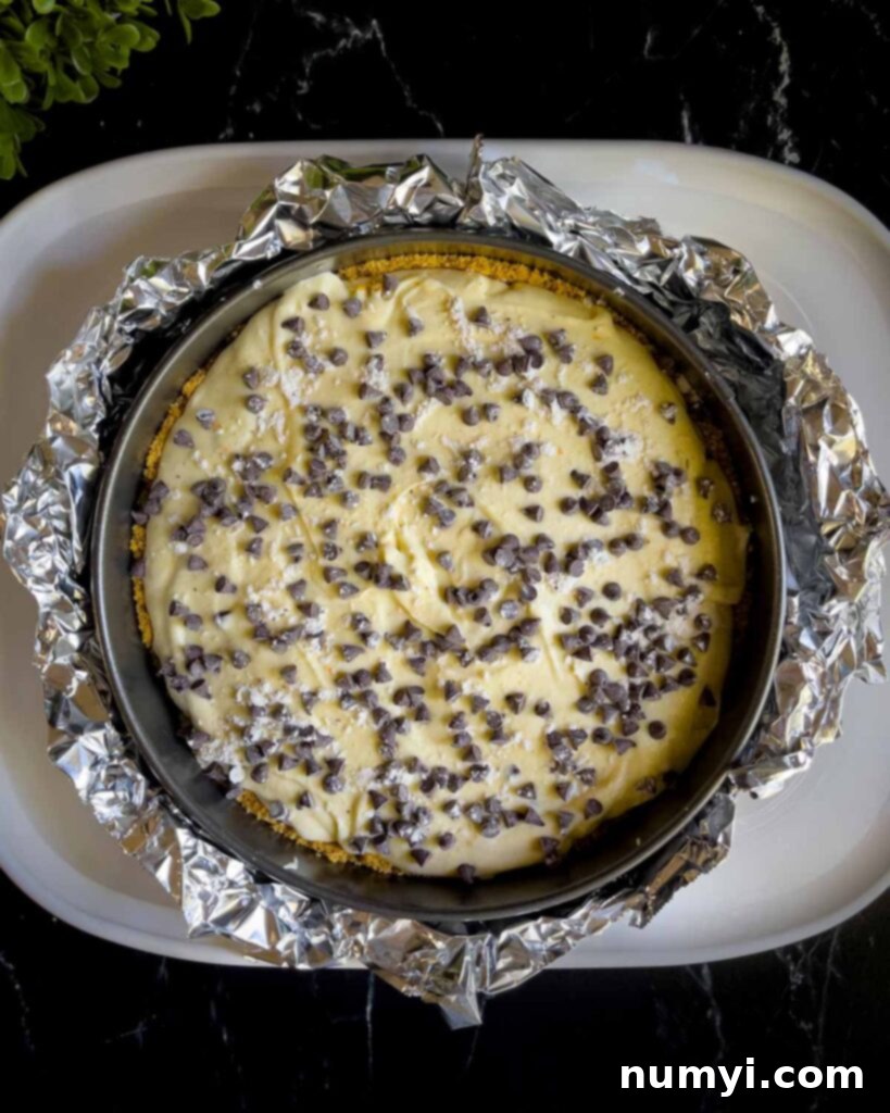 The springform pan, wrapped in aluminum foil and filled with cannoli cheesecake batter, carefully placed inside a larger roasting pan for a water bath.