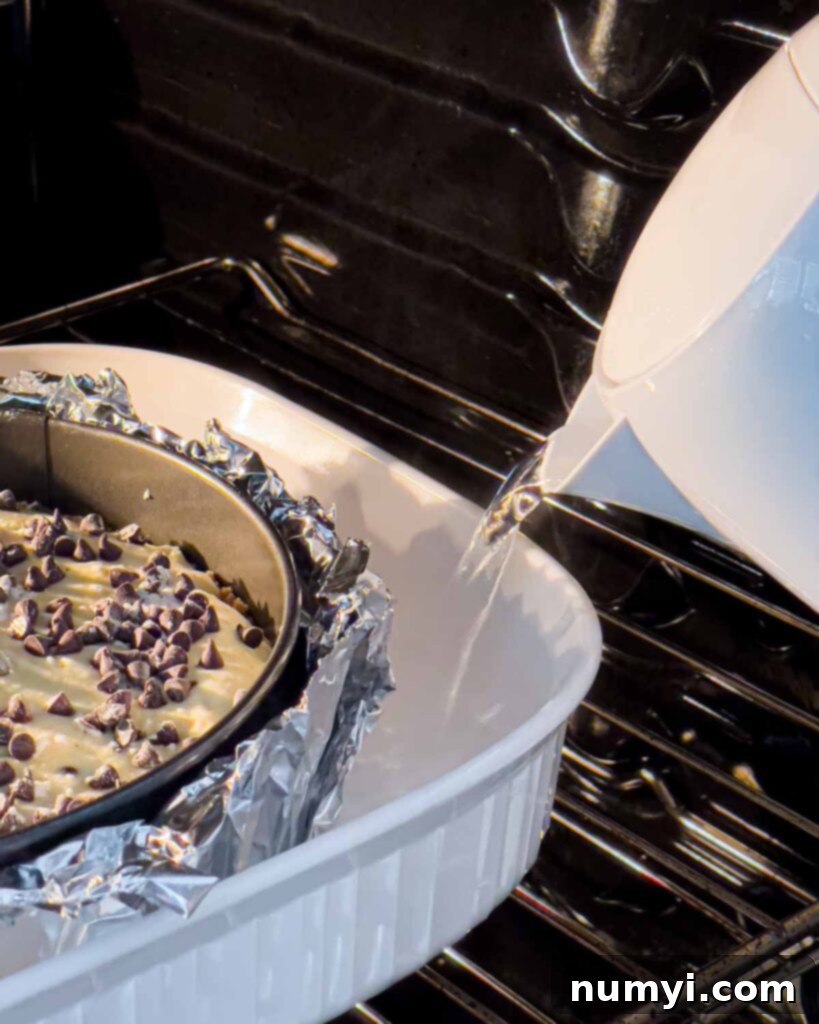 Boiling water being carefully poured into the roasting pan around the springform pan, creating a water bath for the cheesecake in the oven.