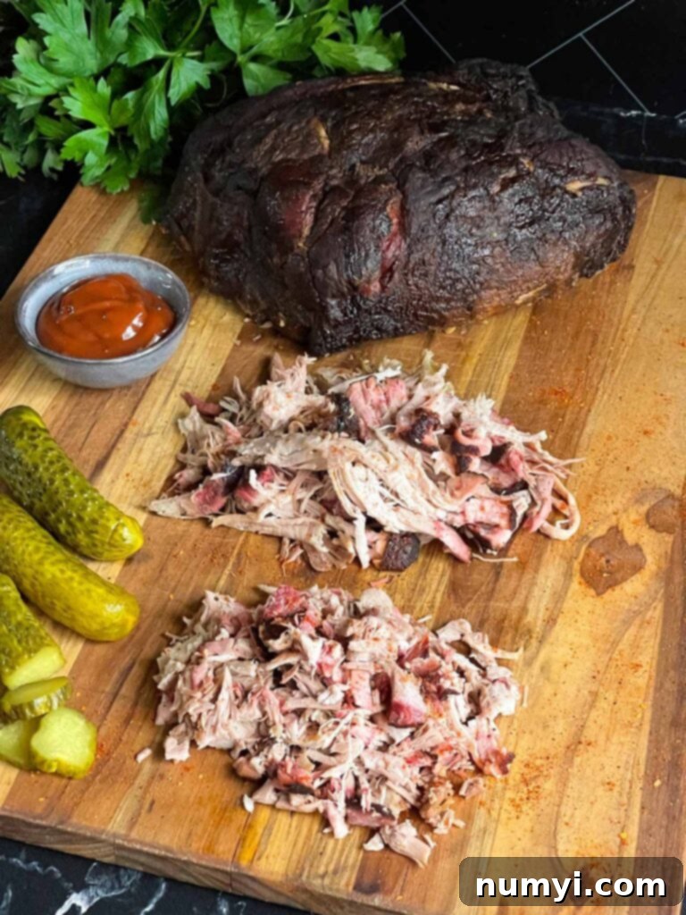A cutting board with a whole smoked pork butt, shredded smoked pork butt, and chopped smoked pork butt.
