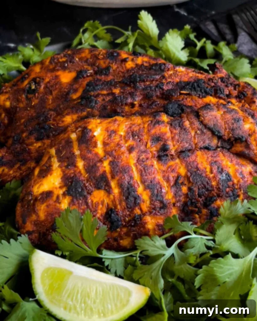 Appetizing Mexican grilled chicken breast (Pechuga Asada) resting on a bed of fresh cilantro, showcasing perfect grill marks.